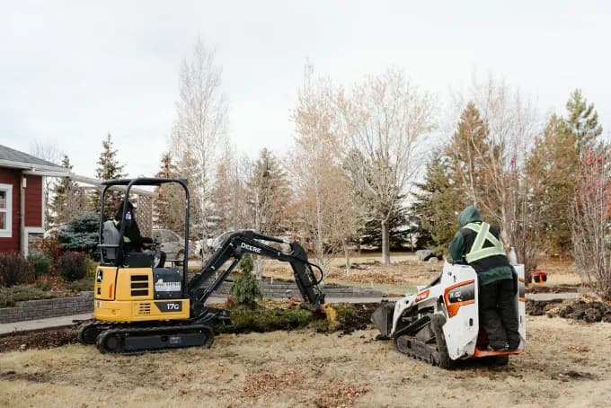 A mini excavator and a compact track loader working in a residential yard